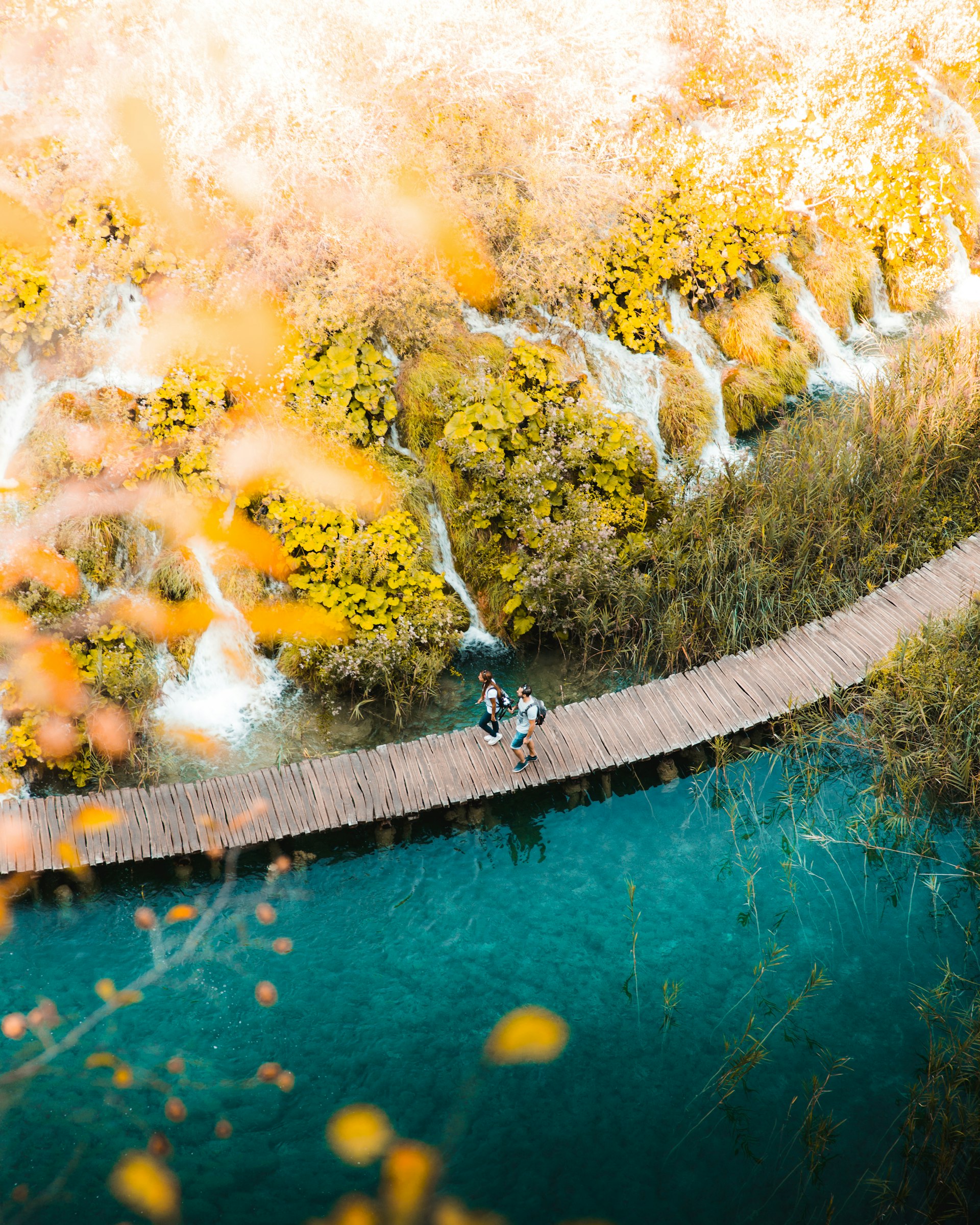 Two visitors walking on boardwalk over turquoise water at Plitvice Lakes in autumn