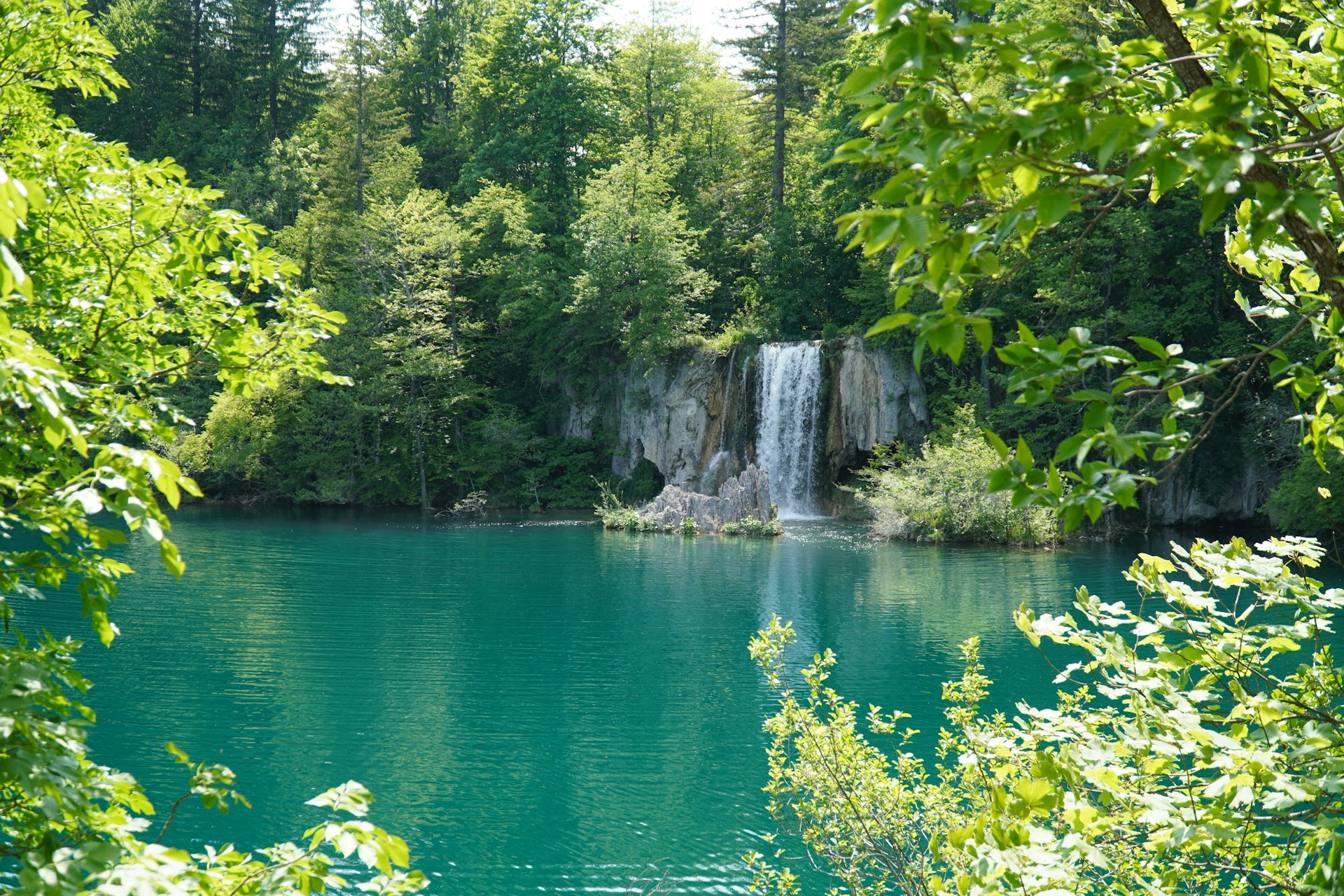 Multiple cascading waterfalls through green trees at Plitvice Lakes in spring